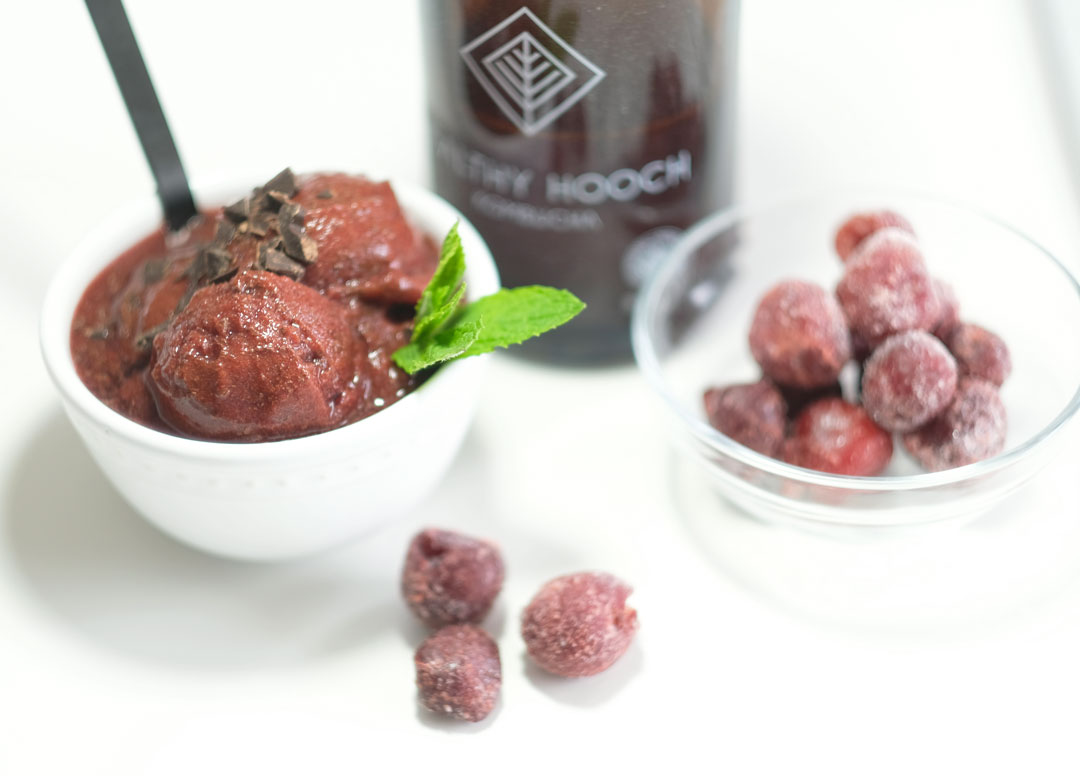bowl of chocolate cherry sorbet next to some cherries and a bottle of kombucha