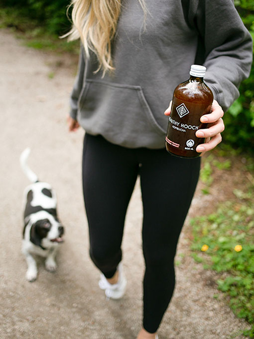 Girl walking her dog in a forest with a bottle of healthy hooch in her hand