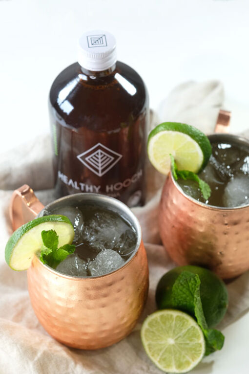 two copper moscow mule glasses with a bottle of healthy hooch kombucha